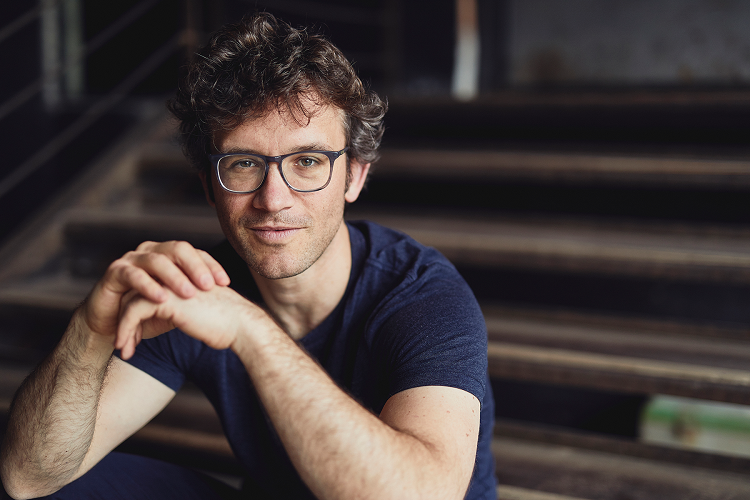Delikatnie uśmiechnięty mężczyzna w okularach patrzący w obiektyw, podpiera łokcie na ławce przed nim - Christoph Altstaedt, fot. Peter Gwiazda_nowe